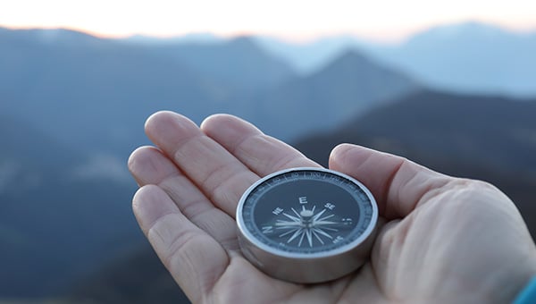 Hand holding a compass mountain top.