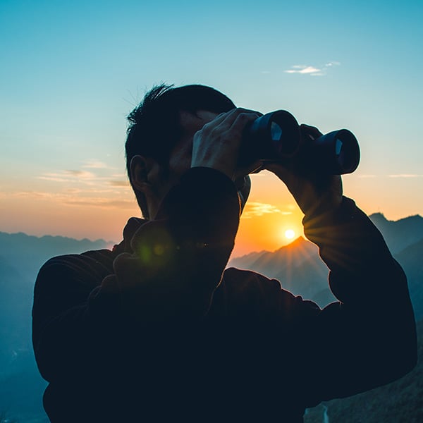 Man wearing binoculars on mountain top.