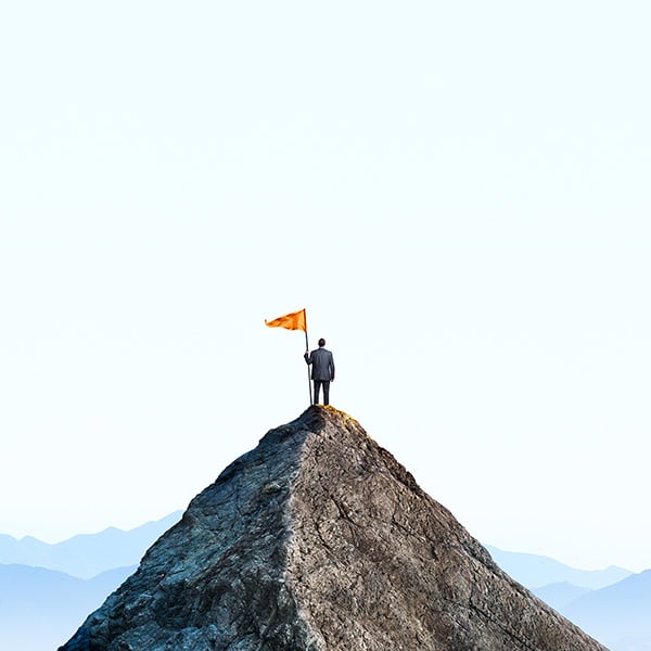 Businessman with flag on mountain top.